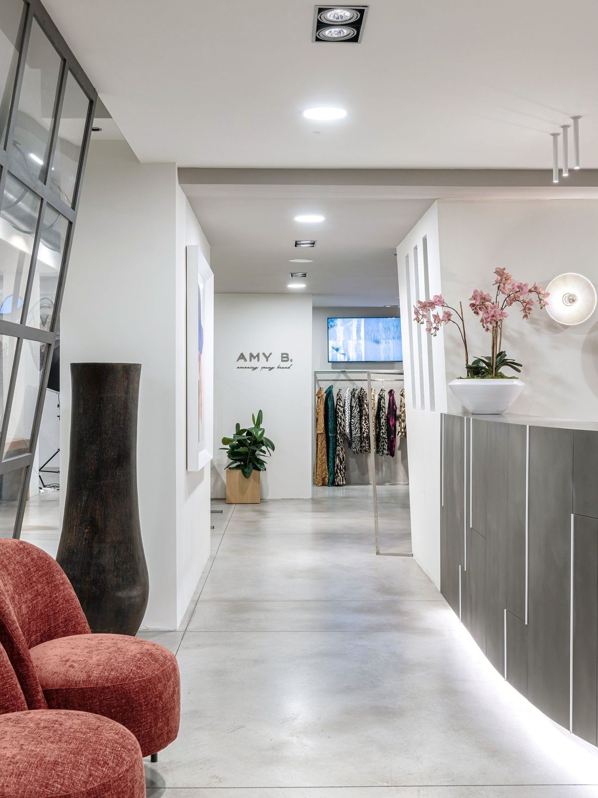 Showroom AMY B., brand di moda donna: corridoio con poltrone rosse, bancone e logo davanti alle collezioni